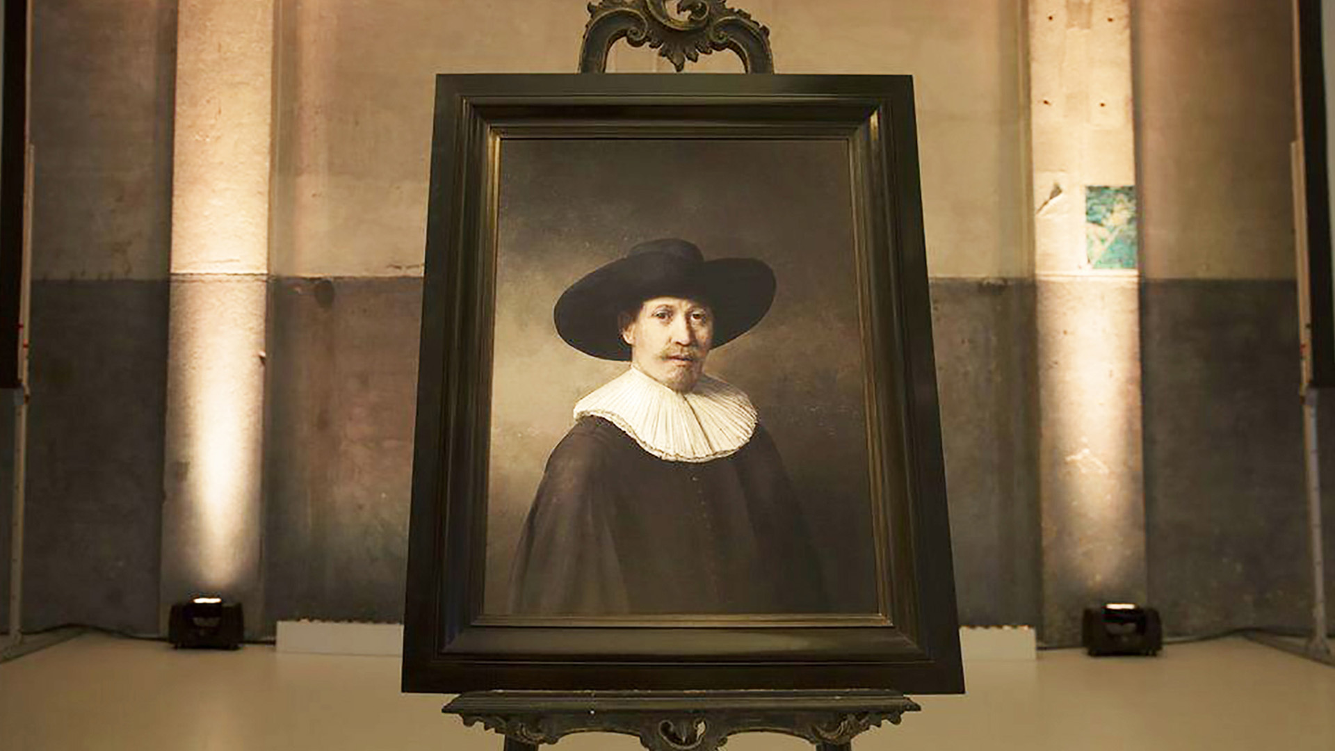 Das von einer KI generierte Gemälde The Next Rembrandt in einem historischen Bilderrahmen auf einer Staffelei, zeigt einen Mann mit breitkrempigem schwarzem Hut und weißem Kragen im Stil Rembrandts.