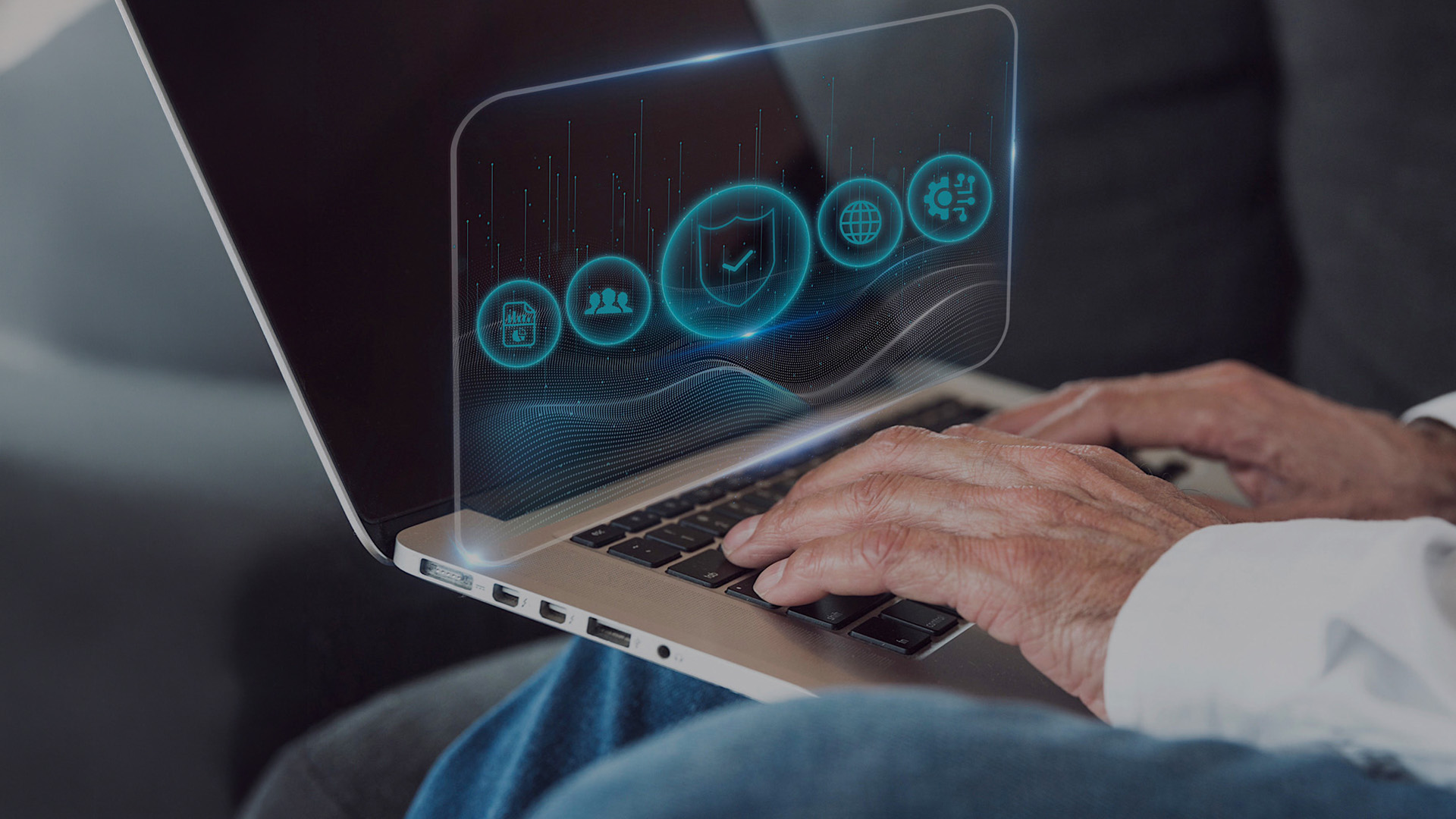 Person tippt auf Laptop, über dem Display schweben transluzente Symbole für Datenschutz und vernetzte Systeme.