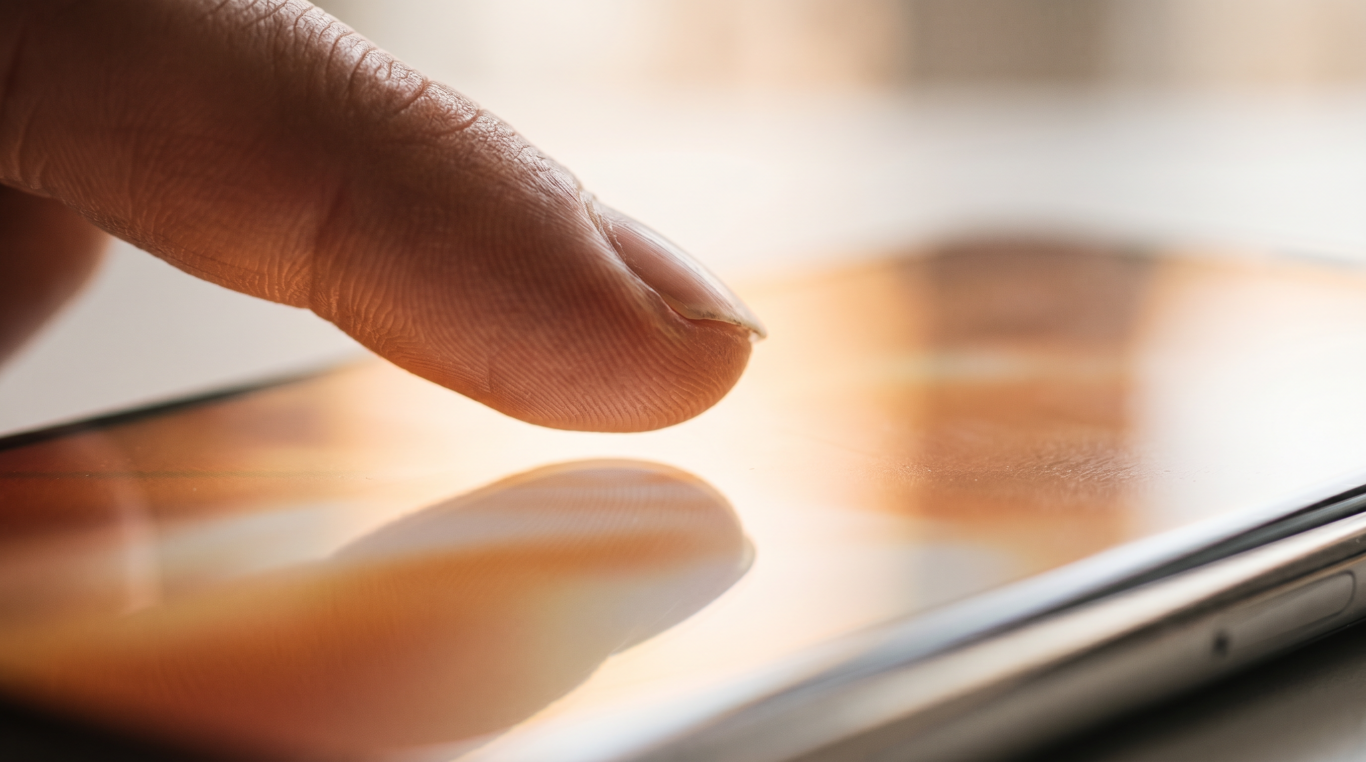Nahaufnahme eines Fingers, der sich der spiegelnden Glasoberfläche eines Smartphones nähert, kurz bevor er den Bildschirm berührt.